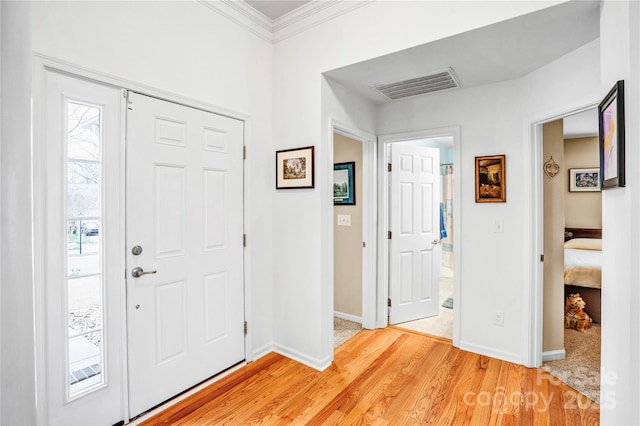 foyer with crown molding, light wood-style flooring, baseboards, and visible vents