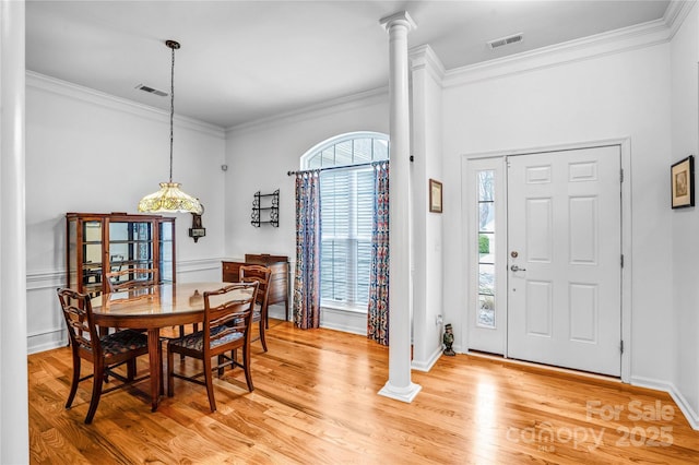 dining area featuring light wood-type flooring, visible vents, crown molding, and ornate columns