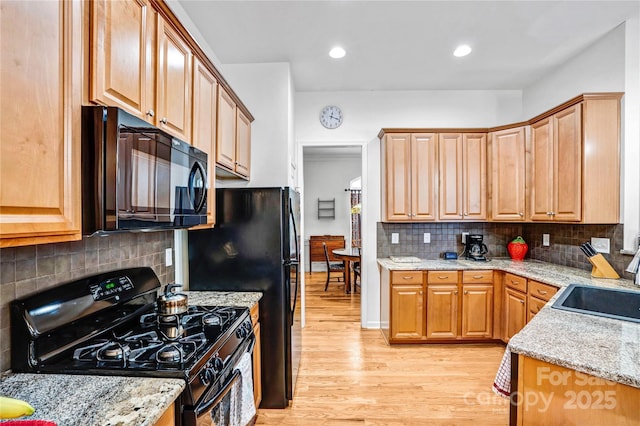 kitchen featuring light stone countertops, black appliances, light wood-type flooring, and a sink