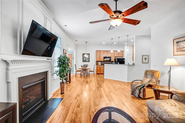 living area featuring a fireplace, light wood-style floors, baseboards, and a ceiling fan