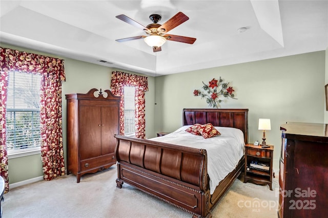 bedroom with baseboards, visible vents, a tray ceiling, ceiling fan, and light carpet