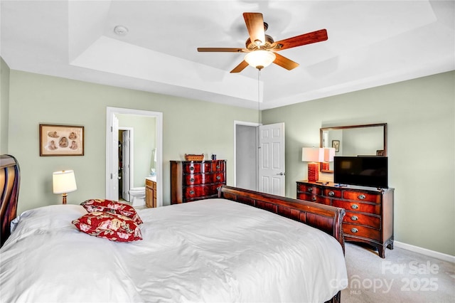 bedroom featuring a ceiling fan, carpet, baseboards, a raised ceiling, and connected bathroom