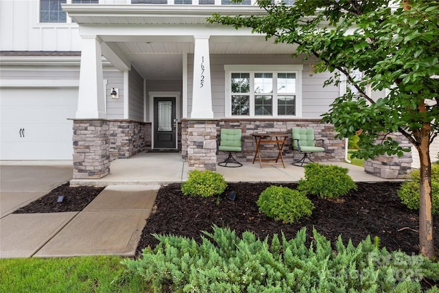 property entrance with covered porch, stone siding, board and batten siding, and a garage