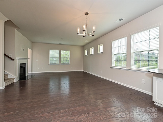 unfurnished living room with dark wood finished floors, a notable chandelier, visible vents, a glass covered fireplace, and baseboards