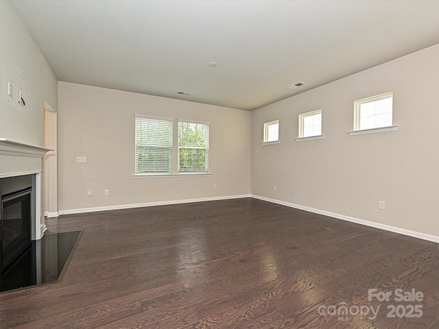 unfurnished living room featuring dark wood-style flooring, a glass covered fireplace, visible vents, and baseboards