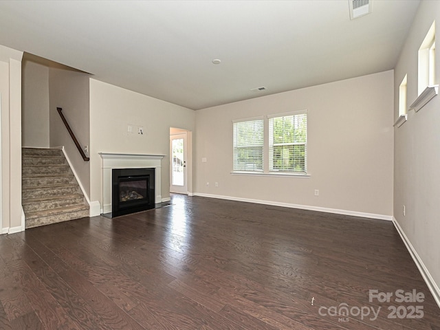 unfurnished living room with stairs, a fireplace with flush hearth, wood finished floors, and visible vents