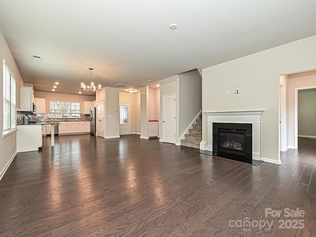 unfurnished living room featuring a chandelier, dark wood-type flooring, a fireplace with flush hearth, visible vents, and baseboards