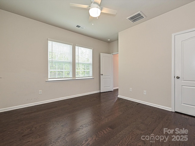 unfurnished room with dark wood-style floors, a ceiling fan, visible vents, and baseboards