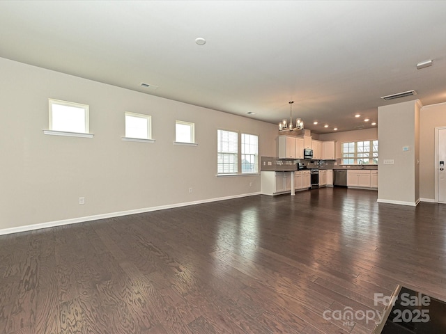 unfurnished living room featuring a healthy amount of sunlight, a notable chandelier, visible vents, and dark wood-style flooring