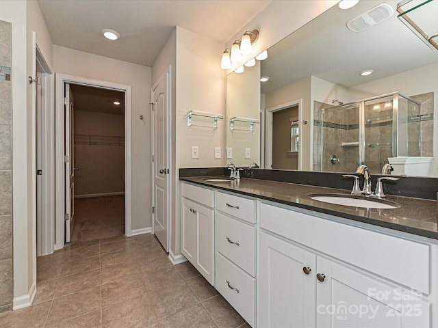 full bathroom featuring tile patterned flooring, a sink, a shower stall, double vanity, and a walk in closet