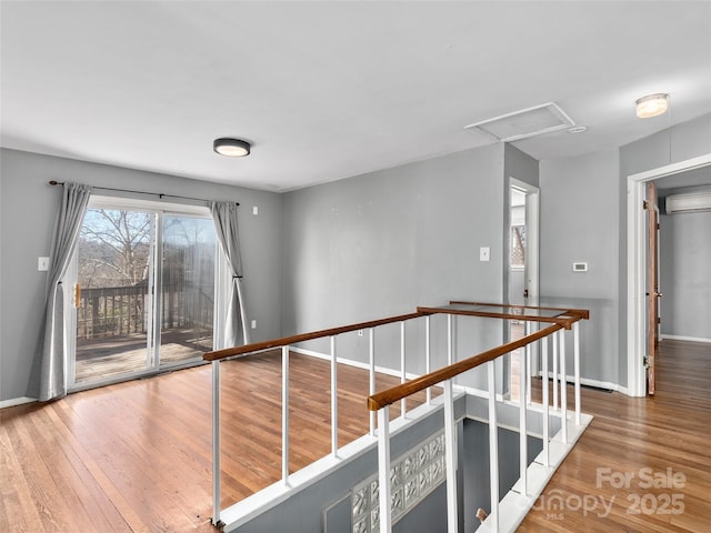 corridor featuring attic access, baseboards, wood finished floors, and an upstairs landing