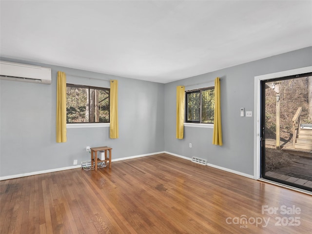 spare room with a wall unit AC, visible vents, baseboards, and wood finished floors