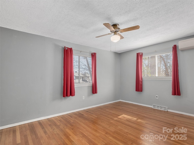 unfurnished room featuring plenty of natural light, visible vents, wood finished floors, and an AC wall unit