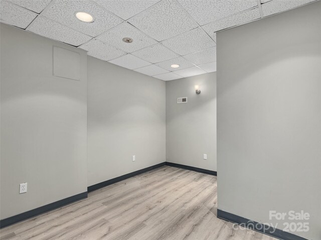 empty room featuring visible vents, a drop ceiling, baseboards, and wood finished floors