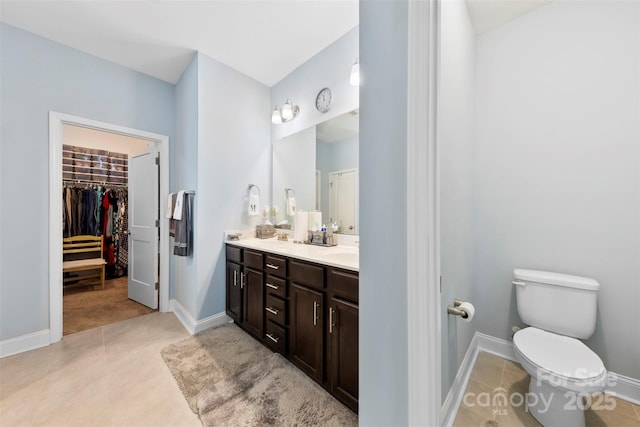 bathroom featuring toilet, baseboards, tile patterned floors, double vanity, and a walk in closet