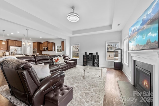 living room featuring recessed lighting, a raised ceiling, a fireplace with flush hearth, wood finished floors, and baseboards