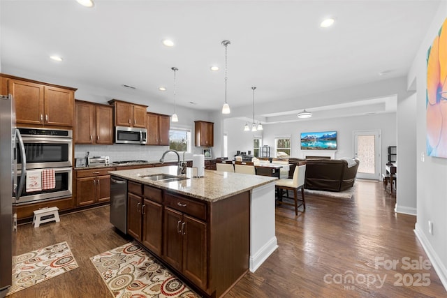 kitchen featuring dark wood finished floors, light stone counters, decorative light fixtures, stainless steel appliances, and a sink