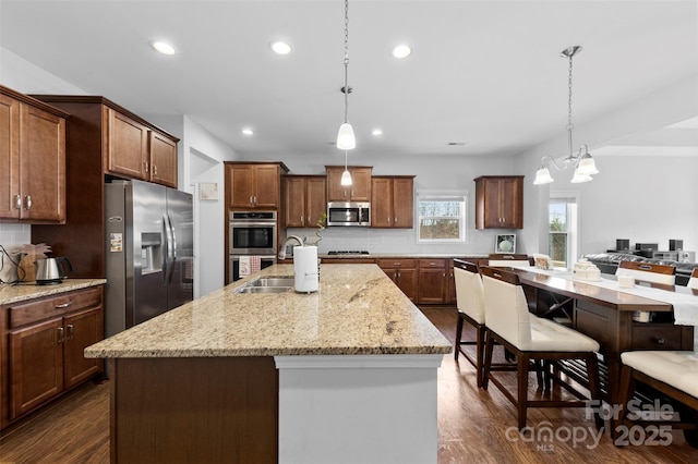 kitchen featuring an island with sink, dark wood finished floors, stainless steel appliances, and a sink