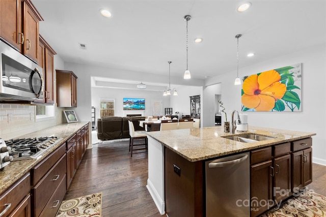 kitchen with dark wood-style flooring, a sink, appliances with stainless steel finishes, tasteful backsplash, and an island with sink