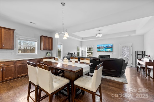 dining room with a tray ceiling, dark wood-style flooring, visible vents, and a fireplace