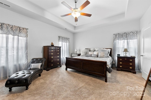 carpeted bedroom with multiple windows, a raised ceiling, visible vents, and a ceiling fan