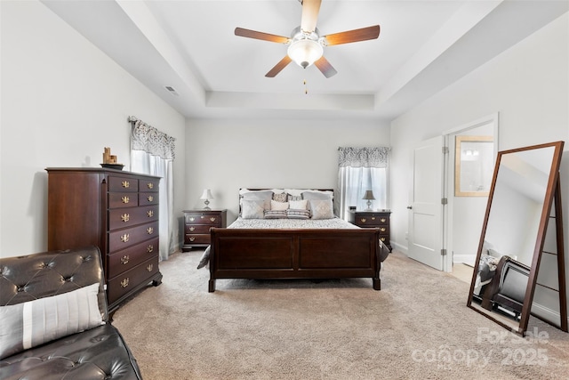 bedroom with light carpet, multiple windows, a raised ceiling, and baseboards