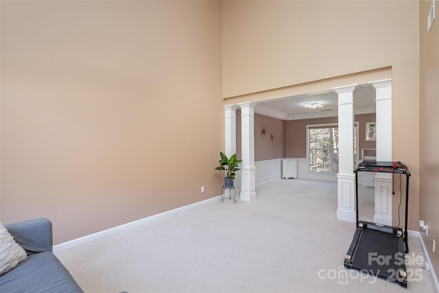 exercise room with crown molding, light carpet, a high ceiling, a decorative wall, and ornate columns