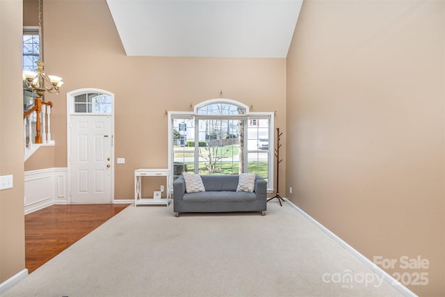 foyer entrance featuring carpet floors, wainscoting, a towering ceiling, wood finished floors, and a notable chandelier