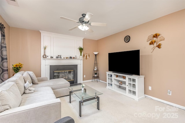 living area with visible vents, light carpet, a glass covered fireplace, baseboards, and ceiling fan