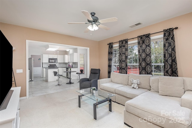 living room featuring visible vents, light colored carpet, and a ceiling fan