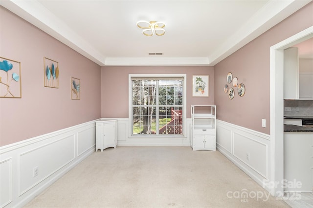 empty room with light carpet, visible vents, and wainscoting