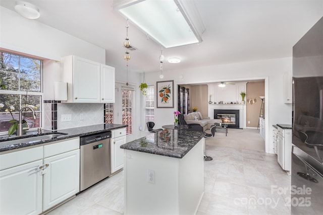 kitchen with a center island, decorative backsplash, stainless steel dishwasher, white cabinets, and a sink