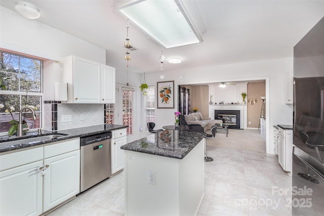 kitchen featuring a glass covered fireplace, white cabinetry, a sink, decorative backsplash, and dishwasher