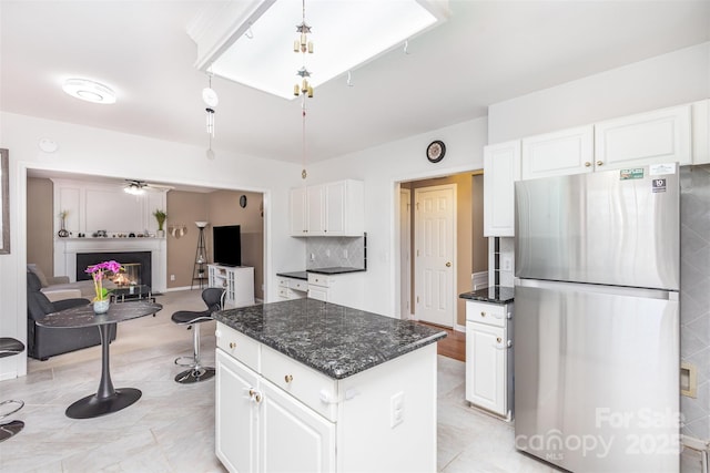 kitchen featuring white cabinets, a warm lit fireplace, a center island, and freestanding refrigerator