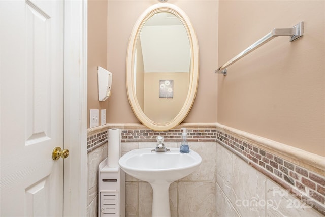 bathroom featuring a wainscoted wall, tile walls, and a sink