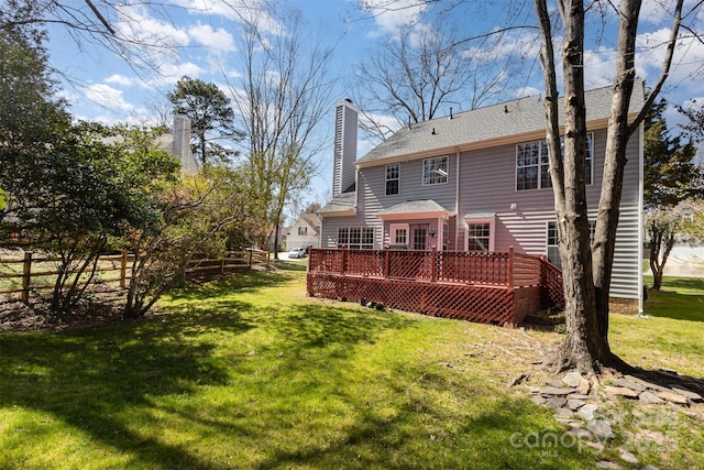 rear view of property featuring a shingled roof, fence, a chimney, a deck, and a yard