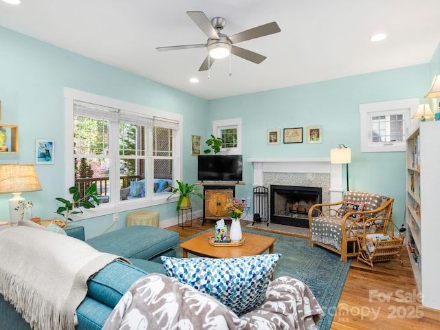 living room featuring baseboards, a fireplace with raised hearth, a ceiling fan, wood finished floors, and recessed lighting