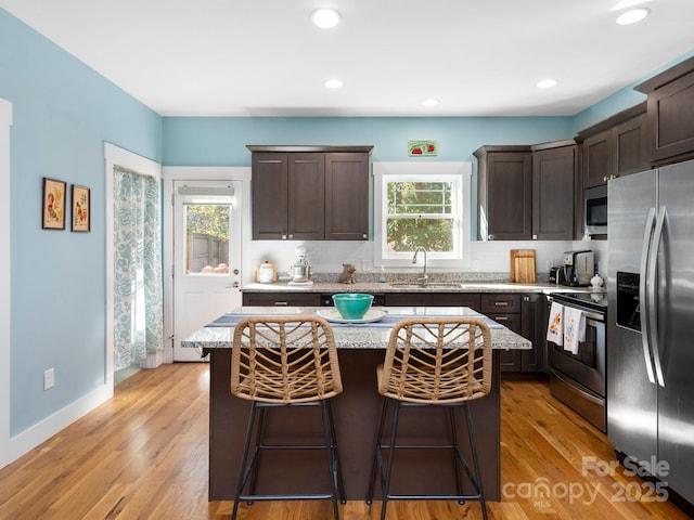 kitchen with appliances with stainless steel finishes, light wood-style floors, a sink, dark brown cabinets, and a kitchen breakfast bar