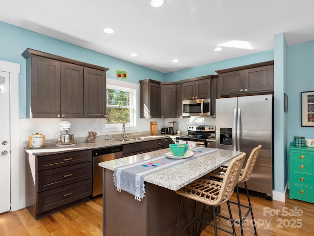 kitchen with a breakfast bar, light wood finished floors, stainless steel appliances, a sink, and dark brown cabinets