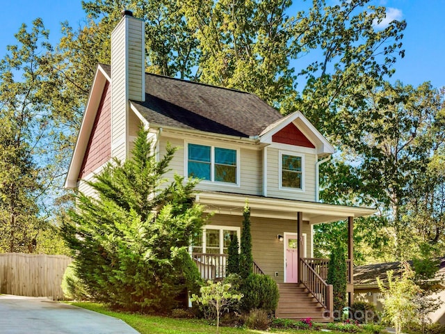 view of front facade featuring covered porch, a chimney, fence, and roof with shingles