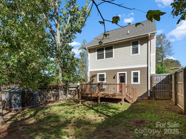 back of property with a fenced backyard, a deck, a lawn, and roof with shingles