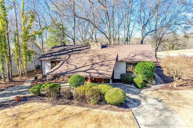 view of front facade featuring driveway, a shingled roof, and a chimney