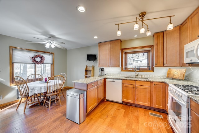 kitchen with a peninsula, white appliances, a sink, visible vents, and decorative backsplash