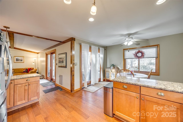 kitchen with light wood finished floors, baseboards, a ceiling fan, light stone counters, and freestanding refrigerator