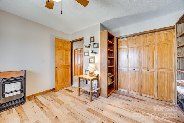 interior space with light wood-type flooring, heating unit, baseboards, and a textured ceiling