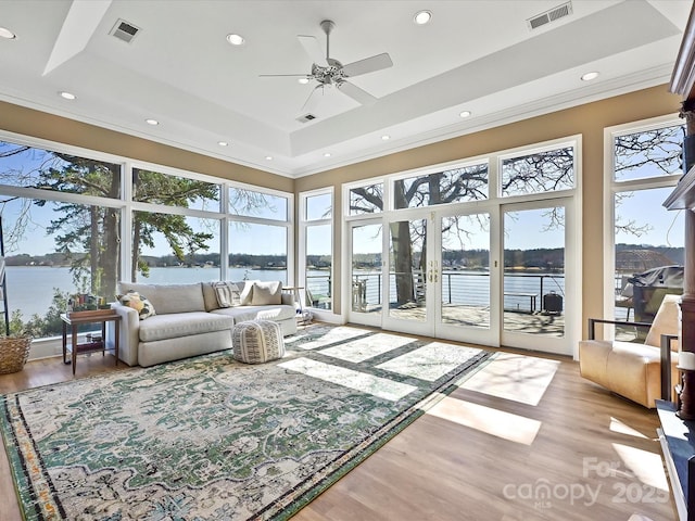 sunroom featuring a water view, visible vents, and a tray ceiling