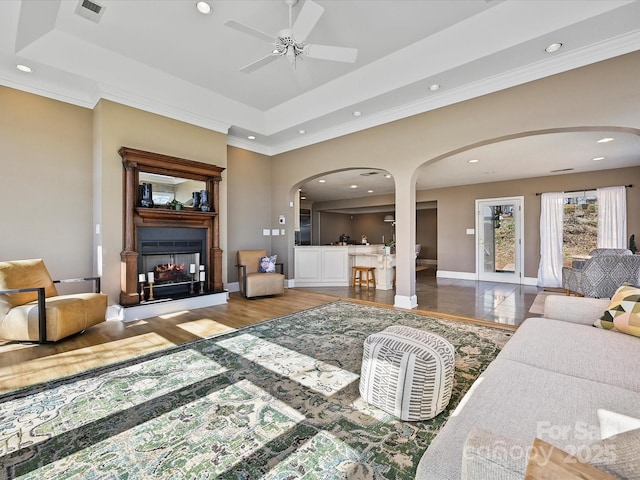 living area with arched walkways, a raised ceiling, visible vents, and a multi sided fireplace