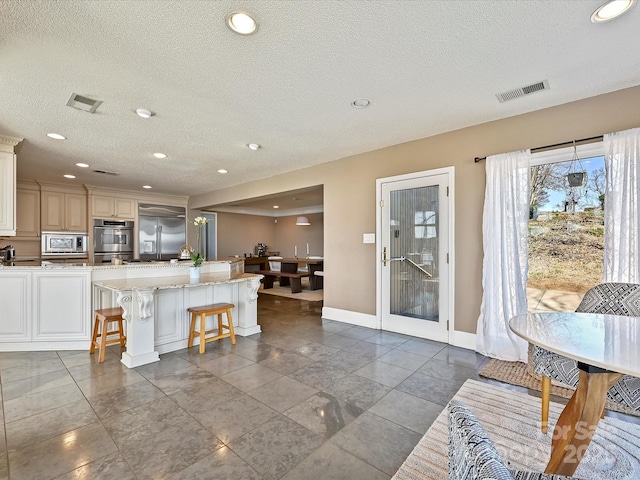 kitchen with visible vents, baseboards, a breakfast bar area, built in appliances, and a textured ceiling