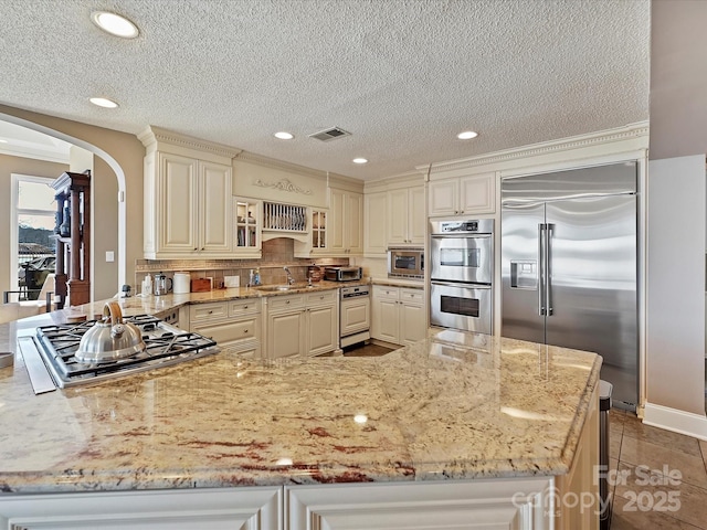 kitchen with visible vents, arched walkways, light stone counters, built in appliances, and a peninsula