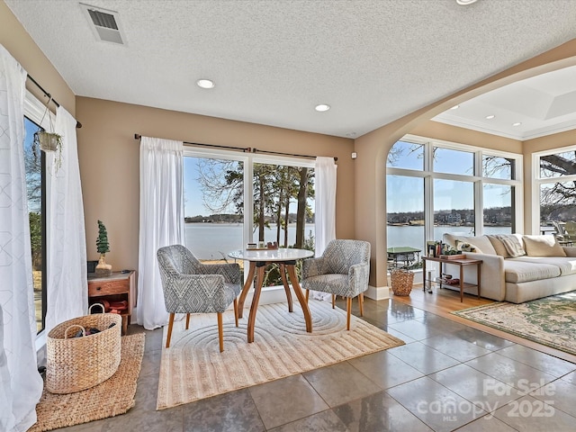 living area with a water view, visible vents, arched walkways, and a textured ceiling